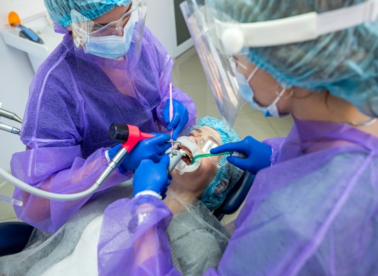 Photo two beautiful helpers in special clothes masks hats gloves help to conduct the operation to the dentist