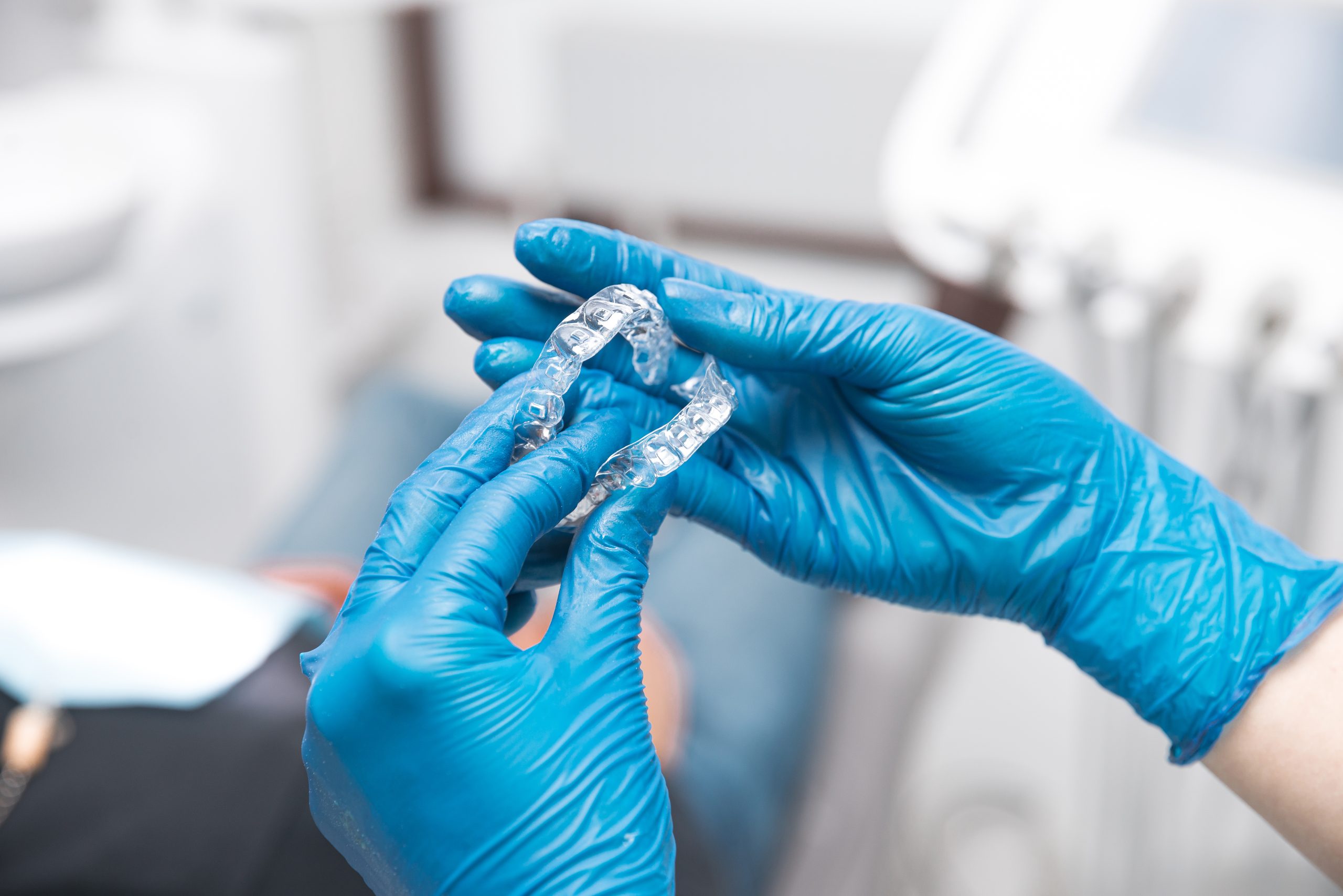 Two women hands wearing blue gloves are holding a pair of invisible aligners Shot in a dental clinic